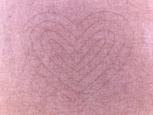 Heart template between a pink cotton fabric and tracing pad.